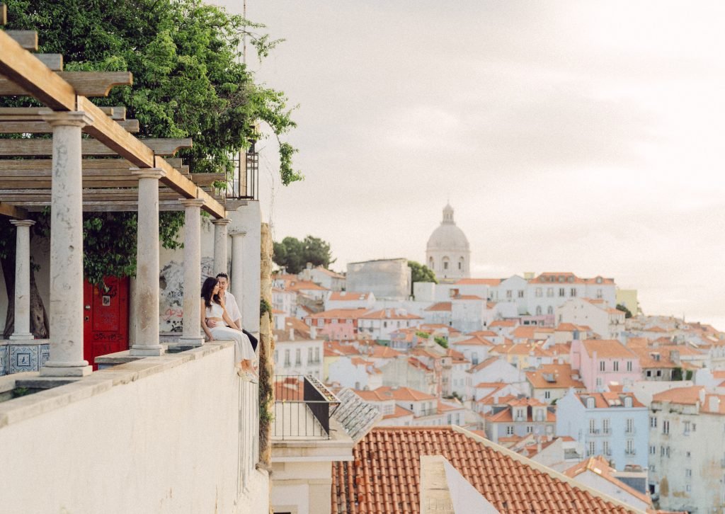 Couple photographed at a Lisbon viewpoint overlooking the Alfama rooftops at golden hour — engagement photographer Flavia Grandi, Lisbon Portugal