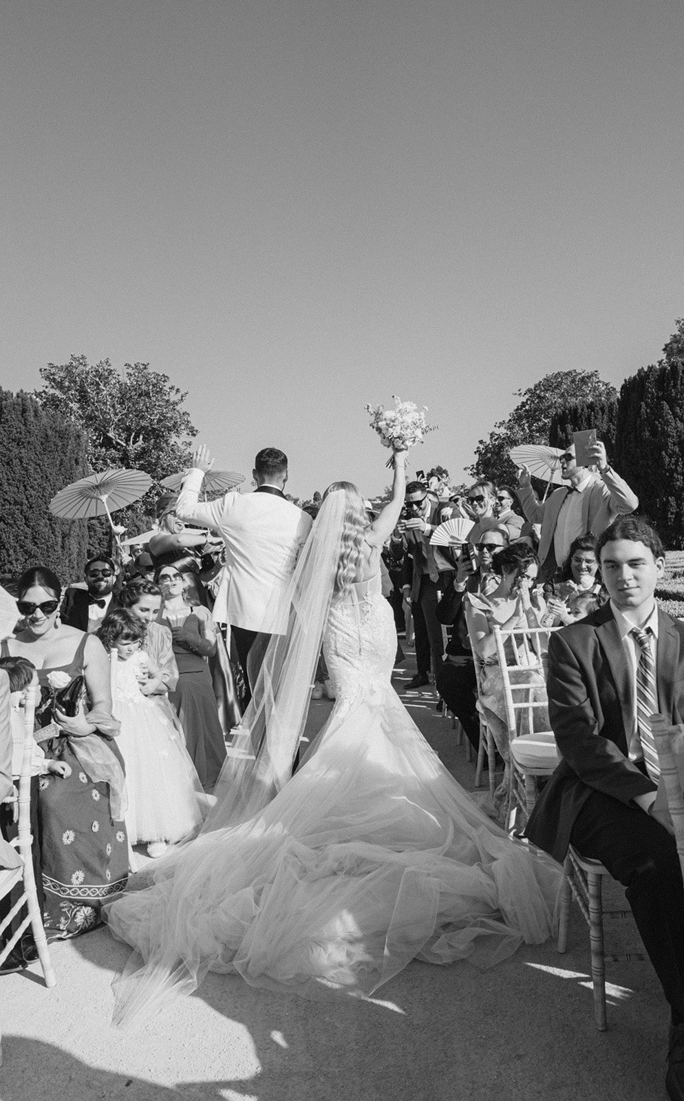 Bride walking triumphantly down the outdoor aisle at a Santorini elopement, veil trailing behind her — elopement photographer Flavia Grandi