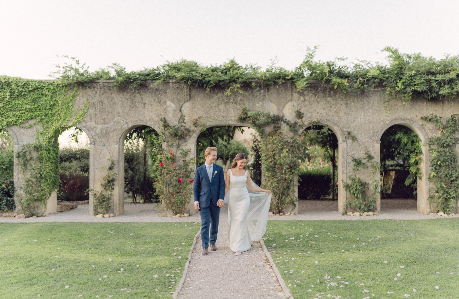 Bride and groom walking through ivy-covered stone arches — Tuscany wedding photographer