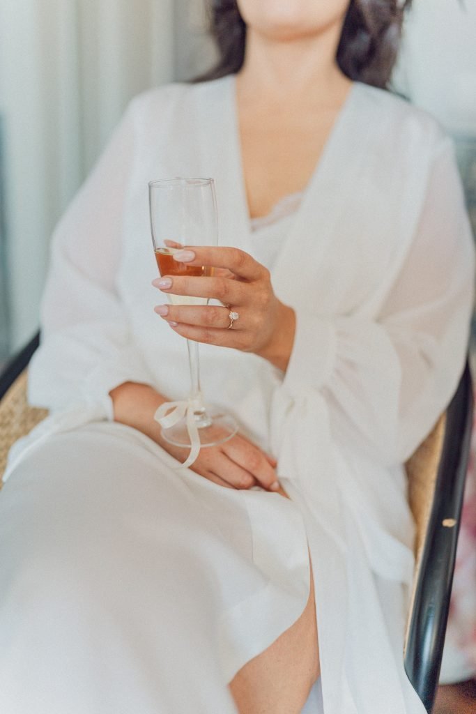 Bride holding champagne and showing engagement ring before wedding