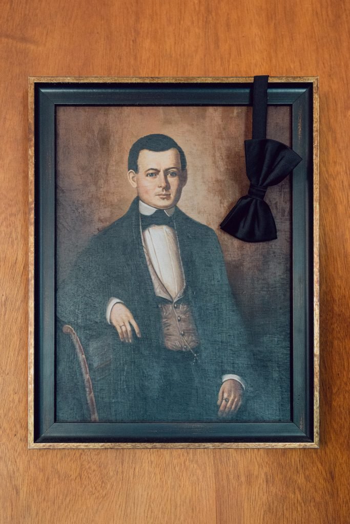 Groom’s black bow tie displayed beside vintage portrait