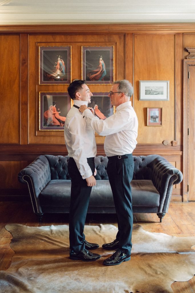 Father helping groom with bow tie before wedding ceremony